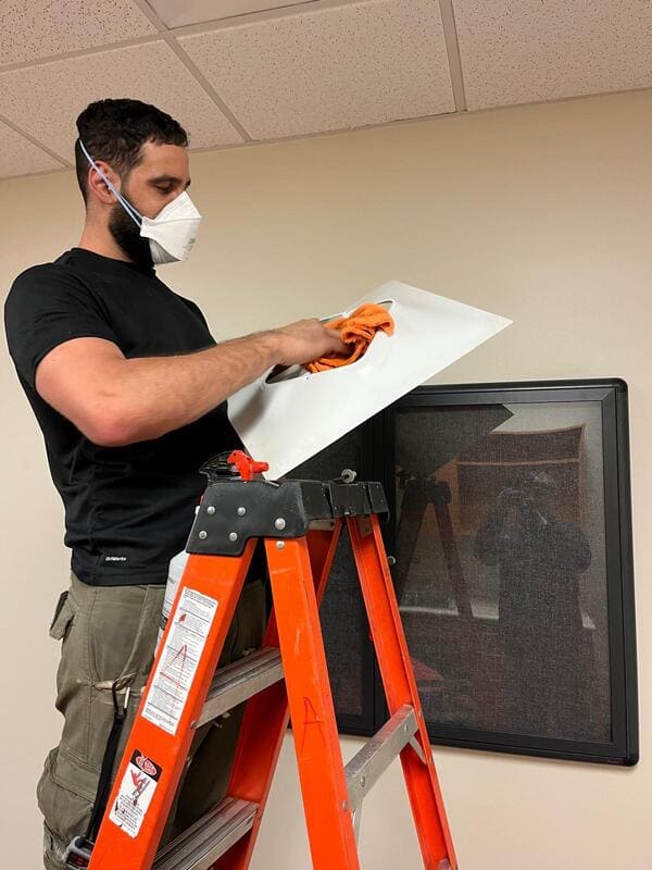 Team member wiping an air vent cover as part of a detailed air duct cleaning process in a commercial clinic – Space Air Duct.