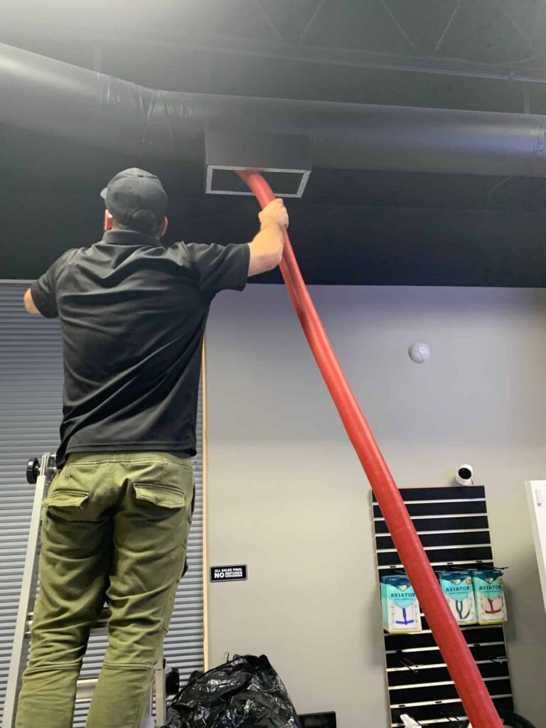 A professional technician from Space Air Duct performing an air duct cleaning service in Dallas, using a high-powered vacuum hose to remove dust and debris from commercial HVAC vents.