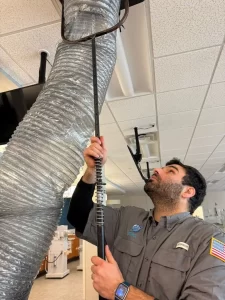 Space Air Duct Cleaning Technician using specialized tools to clean and inspect air ducts in a commercial setting.