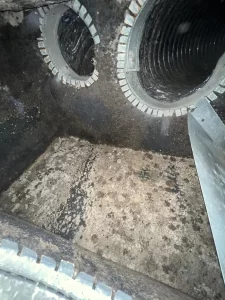 A wide-angle view of the interior of an HVAC plenum box showing heavy accumulation of dark, patchy mold and dust across the fiberglass insulation and surrounding metal surfaces near the duct openings