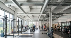 A bustling modern gym with a high ceiling, large windows, and exposed industrial ductwork.