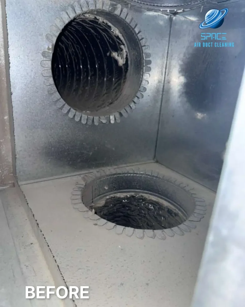 The inside of a dirty metal duct box showing two circular openings for air distribution.
